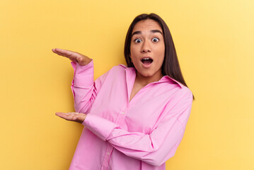 Young mixed race woman isolated on yellow background shocked and amazed holding a copy space between hands.