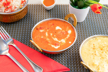 Chicken tikka masala curry on gray tablecloth, topped with red napkin and pilau rice garnish.