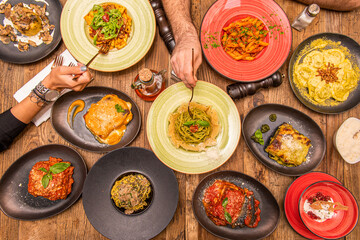 Set of Italian food plates with hands puncturing food. Lasagna, burrata, tagliatelle with pesto, linguine, olive oil, grated Parmesan cheese.