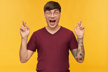 Indoor shot of young male student, keeps his finger crossed with amazed, shocked facial expression....
