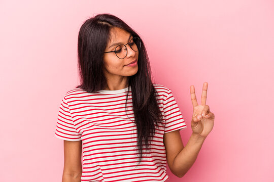Young latin woman isolated on pink background joyful and carefree showing a peace symbol with fingers.