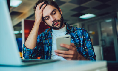 Unhappy male freelancer feeling headache while reading received web message with bad news about...
