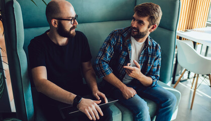 Young male colleagues with laptop computer discussing web projecting during collaborative brainstorming in coworking space, Caucasian programmers talking about software developing on netbook