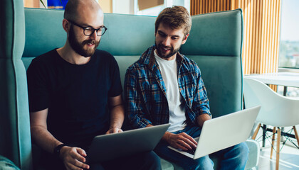 Caucasian IT professionals using modern laptop computers for sharing media files via bluetooth connection browsing website in coworking space, skilled remote colleagues discussing banking app
