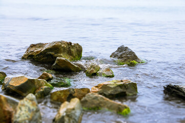 Large moss covered stones on the Black Sea coast, soft focus, waves on a cloudy day