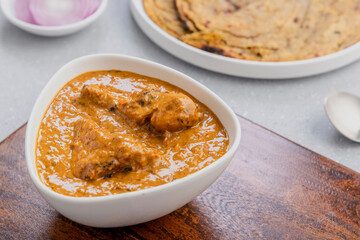 butter chicken gravy served in a white bowl with flatbread roti or naan