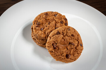Plate of freshly baked chocolate chip cookies. Wooden background, selective focus.