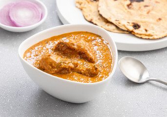 butter chicken gravy served in a white bowl with flatbread roti or naan