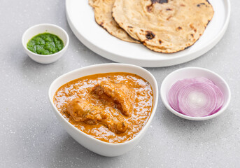 butter chicken gravy served in a white bowl with flatbread roti or naan