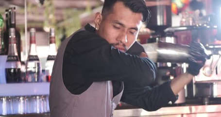 Expert asian bartender shaking cocktail at the bar using metal mixer over colorful background with alcoholic beverages