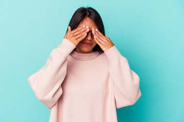 Young latin woman isolated on blue background afraid covering eyes with hands.