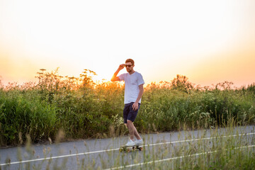 a guy rides a longboard skateboard on the road against the background of the sunset