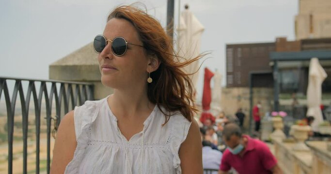 Female Tourist In Sunglasses Sitting Outdoor With Hair Blown By The Wind. medium shot