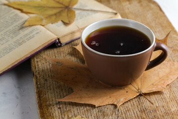 A cup of black tea on a table with a book, dry yellowed leaves of a plane tree