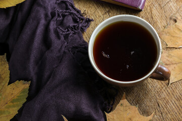 A cup of black tea on a table with a book, dry yellowed leaves of a plane tree and a shawl