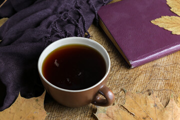 A cup of black tea on a table with a book, dry yellowed leaves of a plane tree and a shawl