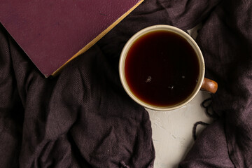 A cup of black tea on a table with a book and a shawl