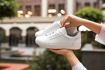 New white sneakers in a female hands at building background - obrazy, fototapety, plakaty