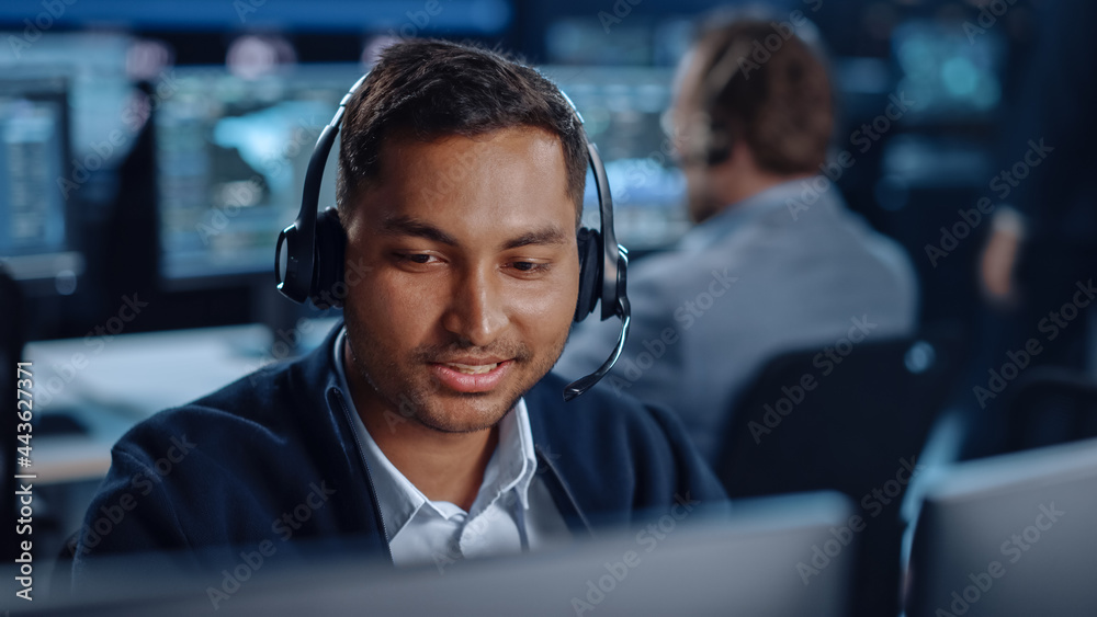 Fototapete Close Up Portrait of a Joyful Technical Customer Support Specialist Talking on a Headset while Working on a Computer in a Call Center Control Room Filled with Computer Display Screens and Data Servers