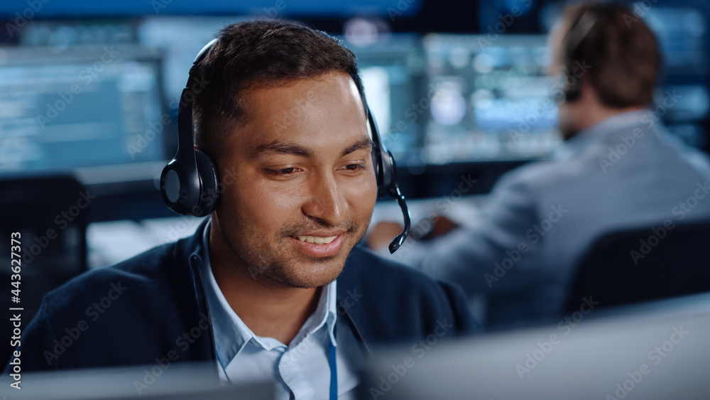 Poster Close Up Portrait of a Joyful Technical Customer Support Specialist Talking on a Headset while Working on a Computer in a Call Center Control Room Filled with Computer Display Screens and Data Servers