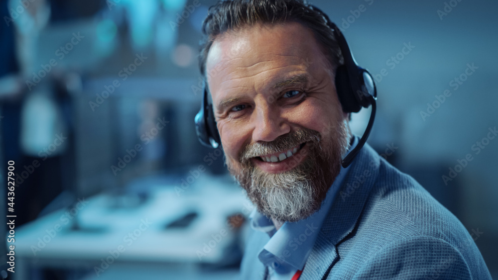 Aufkleber Bearded Happy Senior Technical Support Specialist is Talking on a Headset while Working on a Computer. Successful Employee Turns to the Camera and Gently Smiles. Monitoring Room with Display Screens.