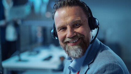 Bearded Happy Senior Technical Support Specialist is Talking on a Headset while Working on a...