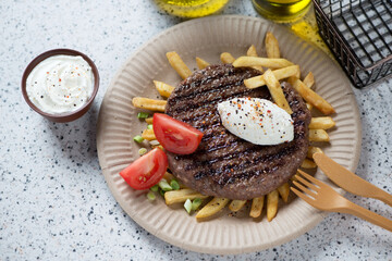 Serbian grilled pljeskavica with kaymak cheese, fries and red tomatoes on a carton plate, studio...