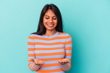 Fototapeta premium Young latin woman isolated on blue background holding something with palms, offering to camera.