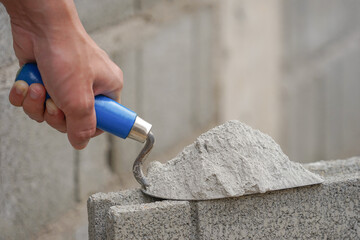hand of industrial bricklayer hold aluminium trowel scoop mortar put on a brick block on construction site with copy space for text, selective focus