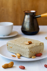 tasty dessert.national traditional sweetness of Turkish and arabic halva with cup of coffee on the table.piece of halwa prepared from sunflower seeds with peanut on the white plate.copy space.vertical