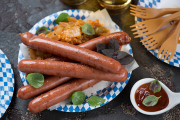 Blue and white carton plate with smoked sausages, stewed cabbage and beer, studio shot on a brown stone background, selective focus