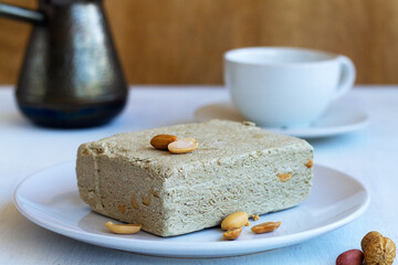 national traditional sweetness of Turkish and arabic halva with cup of coffee on the table. piece of sweet halwa prepared from sunflower seeds with peanut on the white plate. copy space