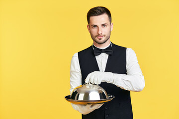 Young handsome waiter holding metal tray with cover ready to serve