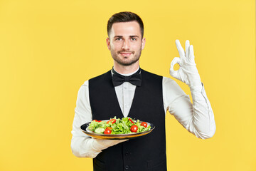 Happy smiling waiter holding plate with healthy vegetable salad doing ok sign with hand and fingers...