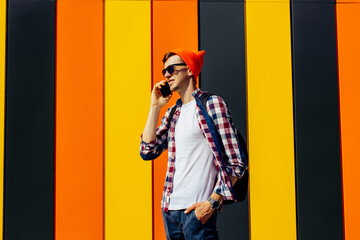 young man walking down the street and looking to the side while talking on the phone against the background of a colorful wall in the city