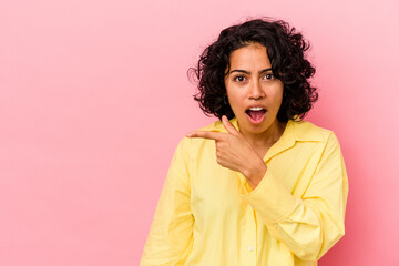 Fototapeta na wymiar Young curly latin woman isolated on pink background smiling and pointing aside, showing something at blank space.