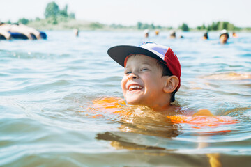 Portrait of a laughing little boy swimming in the water, outdoors. Child learning to swim with the help of life-saving inflatable armbands, cheerful child on an active aqua vacation in the summer