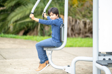 Active kid working out on gym equipment. Fitness concept. Young boy training at park.