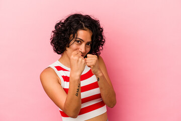 Young curly latin woman isolated on pink background throwing a punch, anger, fighting due to an argument, boxing.