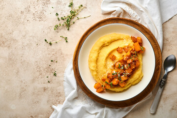 Polenta with butter, pumpkin, garlic, savory and parmesan cheese in white bowl on light concrete background. Traditional Basic Italian food, vegan food. Top view. Copy space.