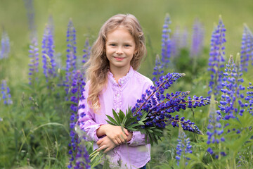 Blonde with flowers in the field.The baby is holding a bouquet of lupines in her hands.A child in the middle of a field collects a bouquet of flowers.Beautiful art picture.A girl with long hair