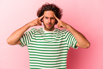 Young caucasian man isolated on pink bakcground focused on a task, keeping forefingers pointing head.