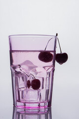 Vertical shot glass of water with cherries and ice cubes.