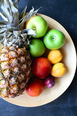 Wooden bowl with various colorful fruit on dark background. Top view.