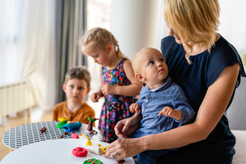 Mother or nursery teacher teaches her children to work with colorful play clay toys