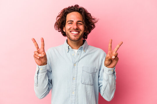 Young caucasian man isolated on pink bakcground showing victory sign and smiling broadly.