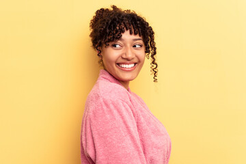 Young mixed race woman wearing a pink bathrobe isolated on pink background looks aside smiling, cheerful and pleasant.