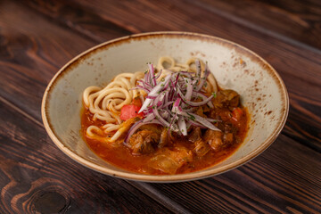 lagman with beef in tomato sauce in a deep plate, photo for the menu