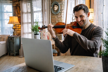 Man student learns to play the violin online using a laptop. © NDABCREATIVITY