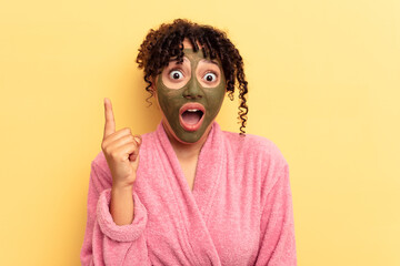 Young mixed race wearing facial mask isolated on yellow background having an idea, inspiration concept.
